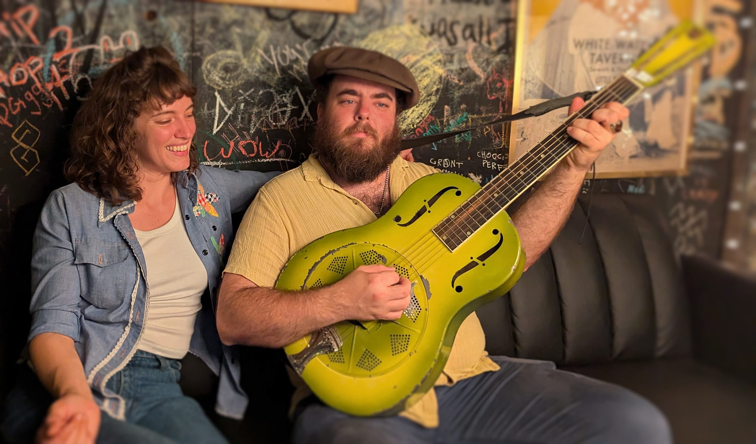 A man and a woman sit together. The man is holding a guitar.