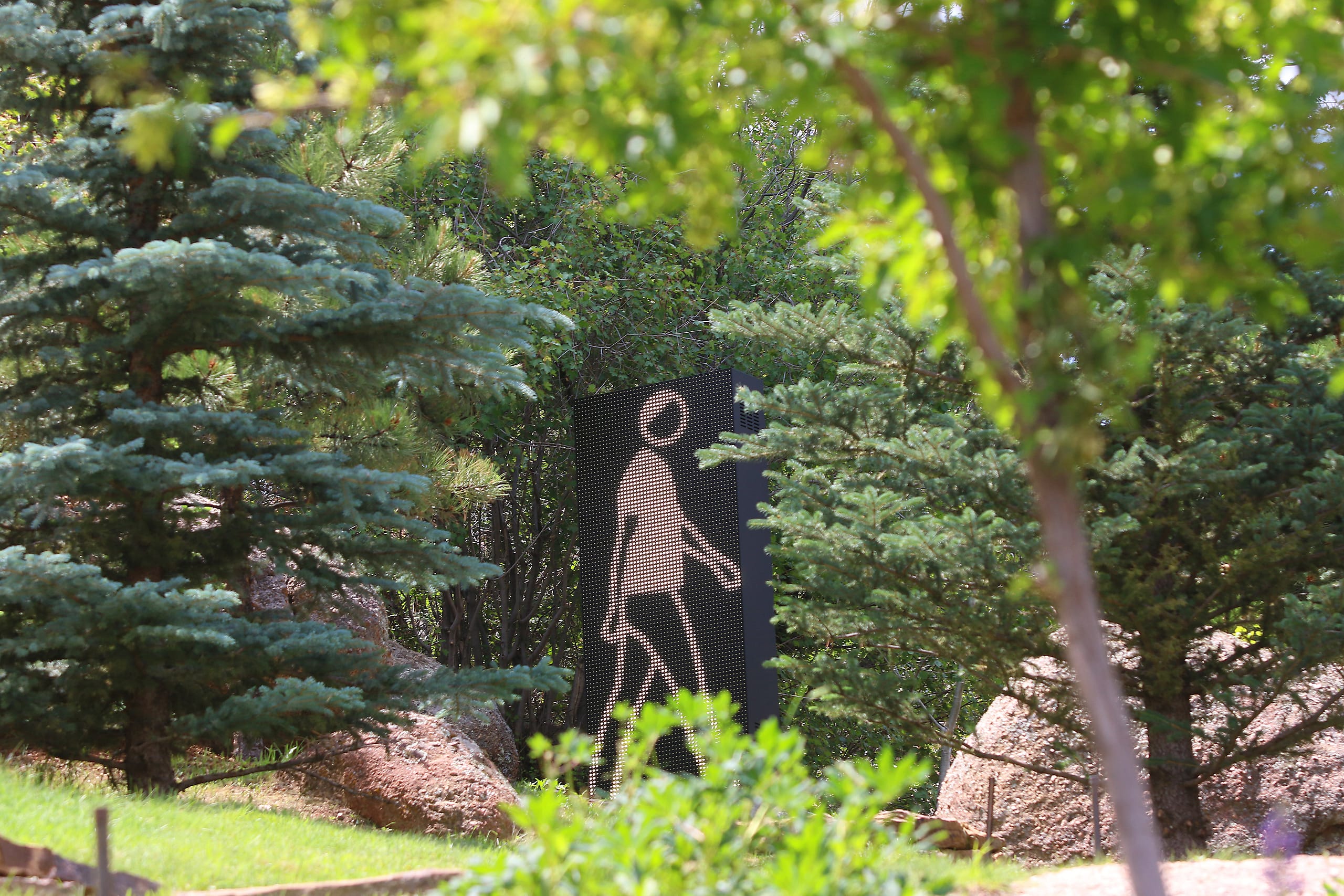 Faime Walking by Julian Opie is set against the backdrop of green trees in the daytime.